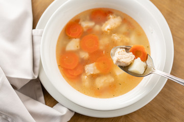 Fish soup in a white plate. Fish soup with vegetables, celery in a cup for the broth. Pike perch and salmon. Plate on wooden table. Restaurant menu