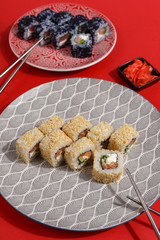 Sushi rolls on colored plates on a red background. A look from above.
