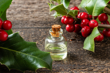 A bottle of essential oil with fresh holly twigs
