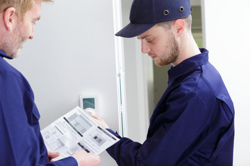 engineer and apprentice adjusting thermostat for efficient automated heating system