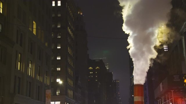 Steam rises and drifts among the rows of buildings along the Fifth Avenue in the night at New York City NY USA during the Christmas Holidays seasons on Dec. 2018.