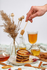 Appetizing pancakes are poured with fragrant honey on the table with tea, dried fruits and nuts.
