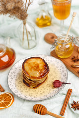 Appetizing pancakes are poured with fragrant honey on the table with tea, dried fruits and nuts.