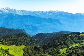 Obraz premium Green mountain ridges, surrounded by high mountains. Snow-capped mountain peaks on the horizon. Krasnaya Polyana, Sochi, Caucasus, Russia.