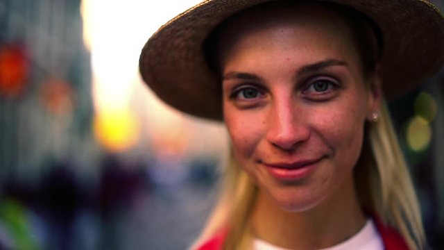 Slow motion   of charming caucasian woman with natural makeup looking at camera, beautiful female standing on street in trendy hat