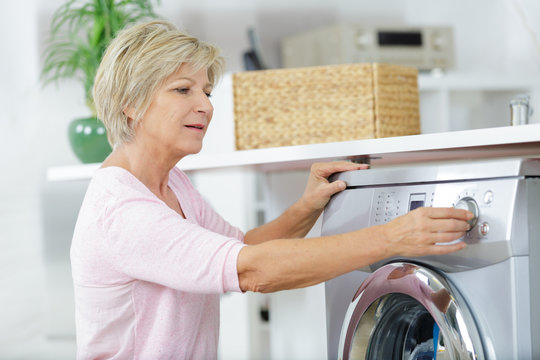 Senior Woman Loading Washing Machine At Home