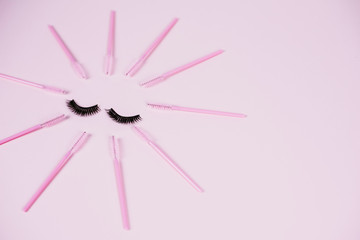 Black fake ribbon eyelashes and brushes for combing extension eyelashes on a pink trendy pastel background. False eyelashes, applicator and brushes. Top view, flat lay
