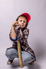 Child boy in jeans and a protective jacket in a red cap with a bat on a white background