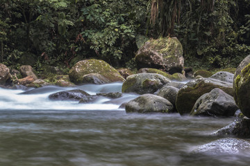 Naklejka na ściany i meble Silk water through rocks in a green costa rican tropical forest. Calmed water in a river