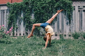 Funny child teenage girl doing cartwheel on a backyard. Excited joyful kid playing outdoor. Happy lifestyle childhood and freedom spirit concept. Seasonal sport activity for children.