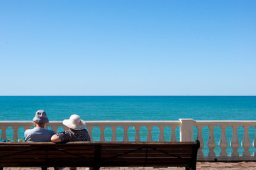 A family or in love couple of adults sits on a bench on the embankment and looks at the sea