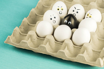 Black egg among angry, prejudiced white eggs attacking the black one. Xenophobic, racist concept.