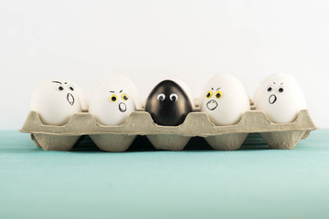 Black egg among angry, prejudiced white eggs attacking the black one. Xenophobic, racist concept. Black lives matter.