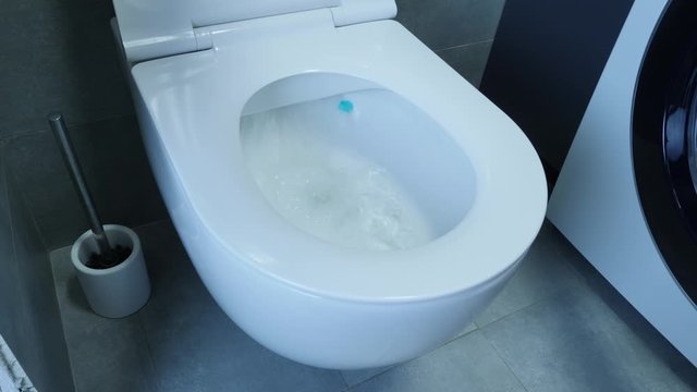 Water flushing down into the toilet bowl in bathroom. Water being flushed in a toilet bowl. Side view of white toilet with flushed water.