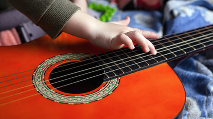 Fototapeta premium children's hand touches the strings on an acoustic six-string guitar. learning to play a musical instrument
