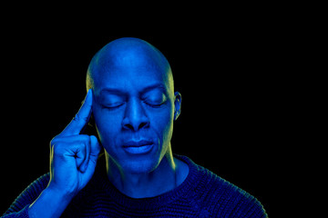 Studio photo with blue light. Black man with eyes closed and thoughtful expression, isolated on black background. Horizontal with copyspace