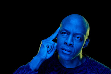 Studio photo with blue light. Black man with thoughtful expression, isolated on black background....