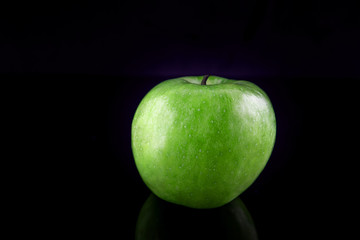 Green apple with reflection, on a black background, shallow depth of field. Concept, healthy food, lifestyle.