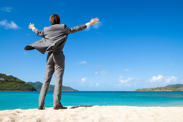 Unrecognizable businessman standing outdoors on tropical beach spreading his arms out into the wind