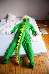 Lounge lizard dinosaur man lying face-down on a double bed on the floor