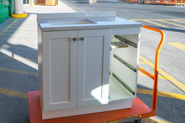 A white cabinet with the drawers removed sits on a trolley cart outside a home improvement store.