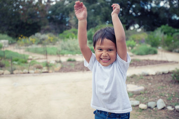 Obraz premium A toddler expressing joy, having fun with his arms raised up and running around on a garden pathway.
