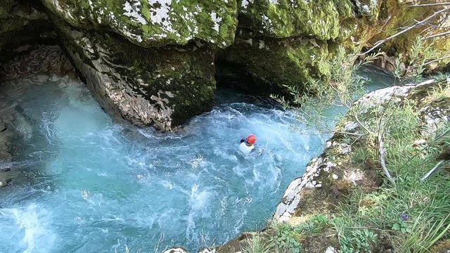 Man doing canyoning jump into the clear blue river from the cliff