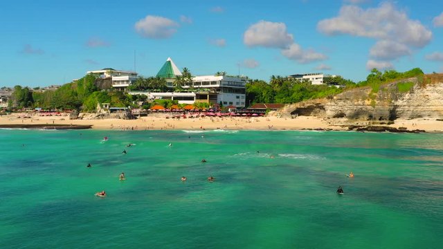 Dreamland beach one of the most beautiful sand beach Bali with happy travel tourist resting under umbrella and surfers in crystal clear sea water. Aerial view. Shot in 4K on Hasselblad, H.265