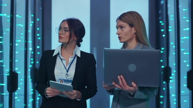 Team of IT specialists women working together at database, inspecting servers supercomputer, running diagnostics using technology in high secure server room. Data center.