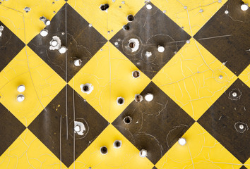 Close up of a yellow and black caution road sign full of bullet holes.