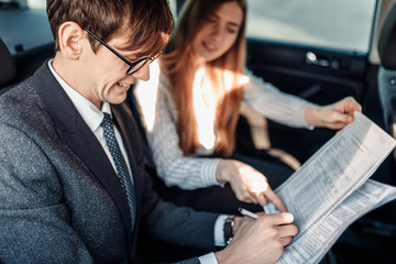 Business man and woman, business partners read documents in the car