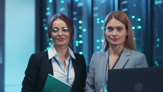 Two female engineers coworking in IT tech environment of secure server room. Couple portrait of beautiful successful women in modern data center.