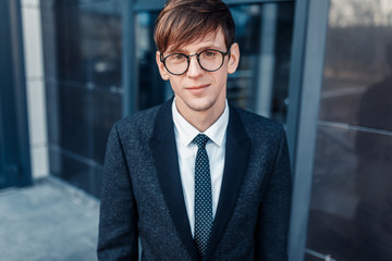 Stylish business businessman in glasses, standing near the glass building of the business center