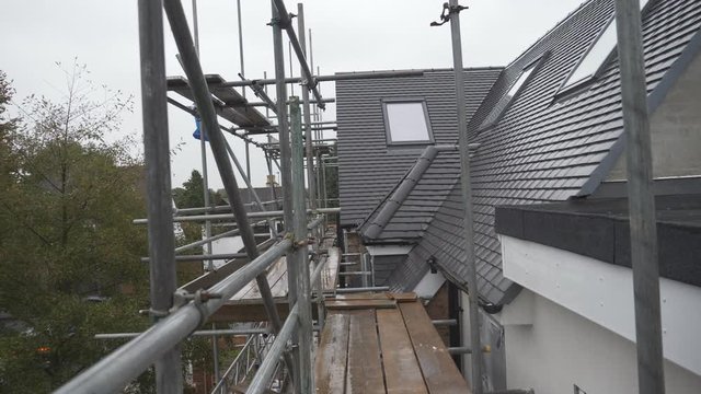 A scaffolding besides roof tiles on a rainy day.