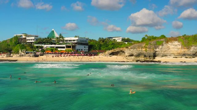 Dreamland beach one of the most beautiful sand beach Bali with happy travel tourist resting under umbrella and surfers in crystal clear sea water. Aerial view. Shot in 4K on Hasselblad, H.265