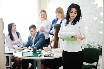 Portrait of caucasian woman in white blouse hold green folder against business people group of bank workers.