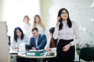 Portrait of caucasian woman in white blouse and eyeglasses speak on mobile phone against business people group of bank workers.