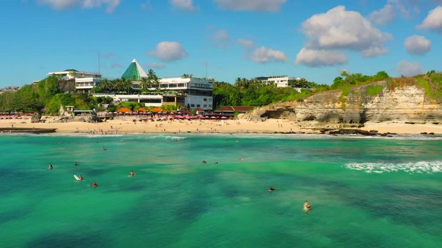 Dreamland beach one of the most beautiful sand beach Bali with happy travel tourist resting under umbrella and surfers in crystal clear sea water. Aerial view. Shot in 4K on Hasselblad, H.265