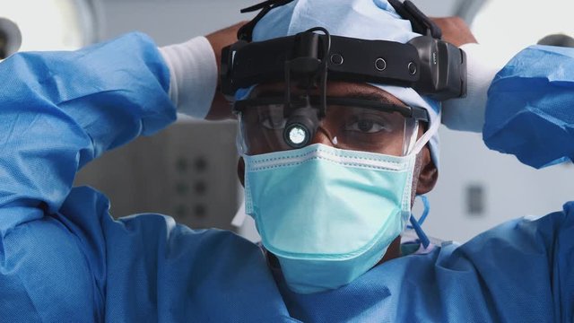Male Surgeon With Protective Glasses And Head Light Putting On Mask In Hospital Operating Theater