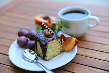 Food background. In the center of the frame on a wooden table is a white plate with a slice of sponge cake and fruit and a cup of coffee. Close-up, side view, horizontal, place for text. Food concept.