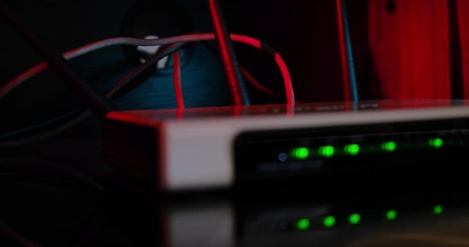 Home internet router on reflective surface with out of focus blinking green led lights, visible UTP cables and antenas, red light in the background. Close up shot.