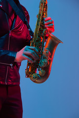 Obraz premium Young caucasian jazz musician playing the saxophone on gradient blue-purple studio background in neon light. Concept of music, hobby, festival. Joyful attractive guy. Colorful portrait of artist.