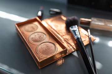 Gold palette with blush on a glass table. Professional makeup set: eyeshadow palette, blush, powder, make-up brushes, many cosmetics closeup.