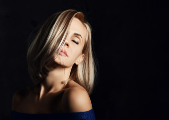 Naklejka premium Sensual blonde beautiful woman mysteriously thinking posing in fashion blue dress on a dark