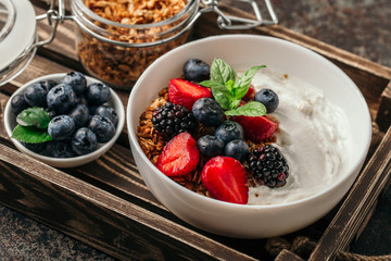 Healthy breakfast with granola, yogurt, fruits, berries on dark metal background. Summer homemade breakfast.