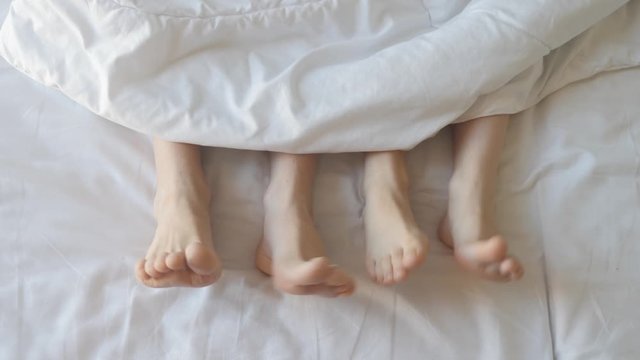 Two pair of feet next to each other in a bed. Mother and daughter lie on bed with white sheets.