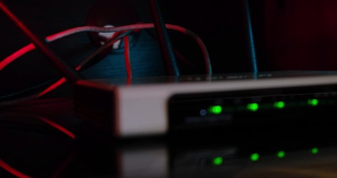Network Router with out of focus green led lights and red light sweeping from side to side in the background, with visible UTP internet cables and router antennas. Close up.