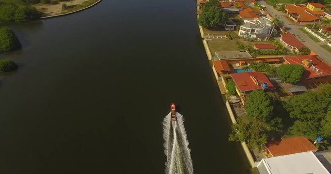 Drone shot following a small red fishing boat on a dark water canal in Higuerote, Venezuela