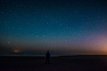 Adventurous man watching the stars on a beach at night.  - obrazy, fototapety, plakaty