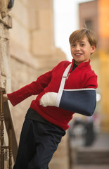Smiling blond boy with bandaged arm with plaster and sling. Left arm fracture. kids being kids